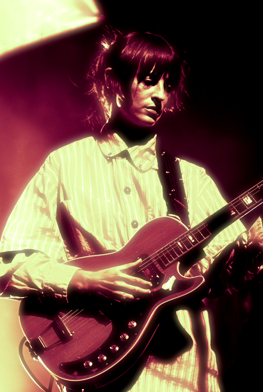 Guitarist in white shirt playing a vintage guitar under purple lighting